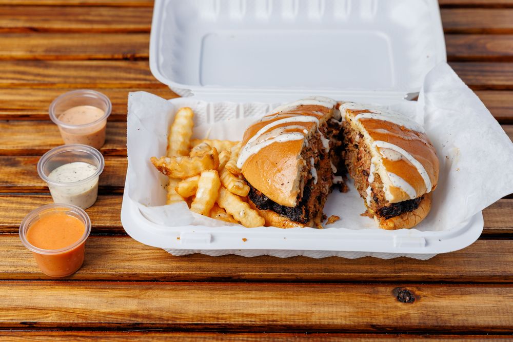A chapli kabab burger in a bun, cut in half, served with fries.