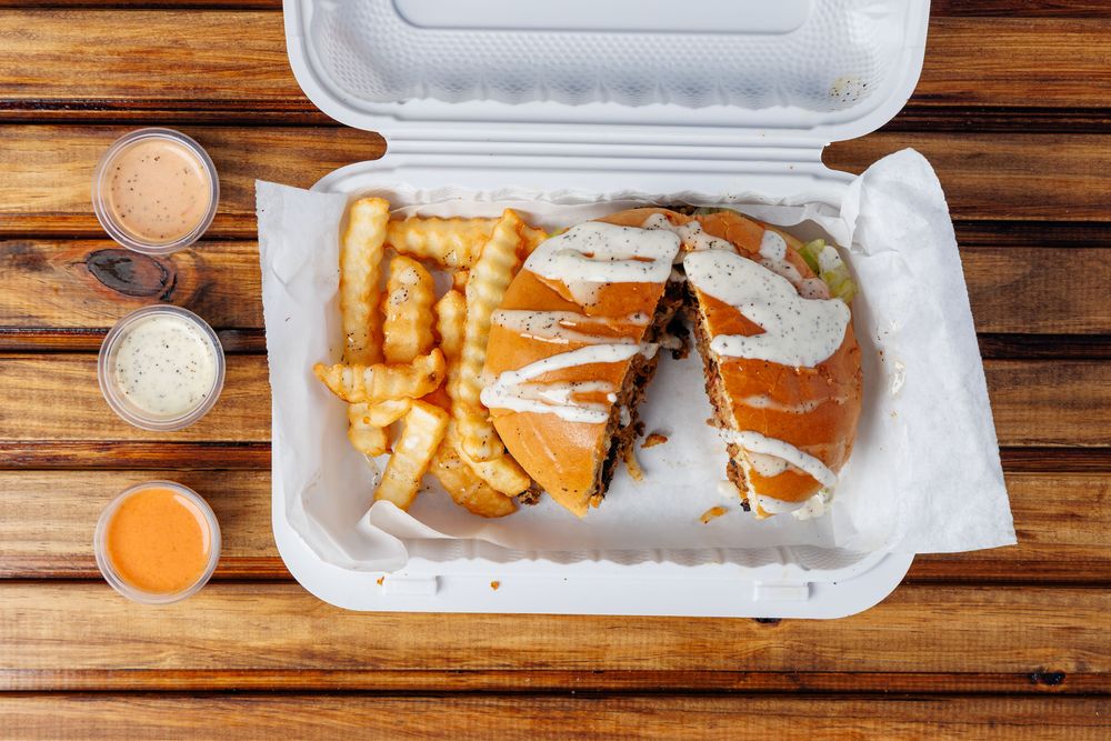 A chapli kabab burger in a bun, drizzled with white sauce and cut in half, served with crinkle-cut fries.