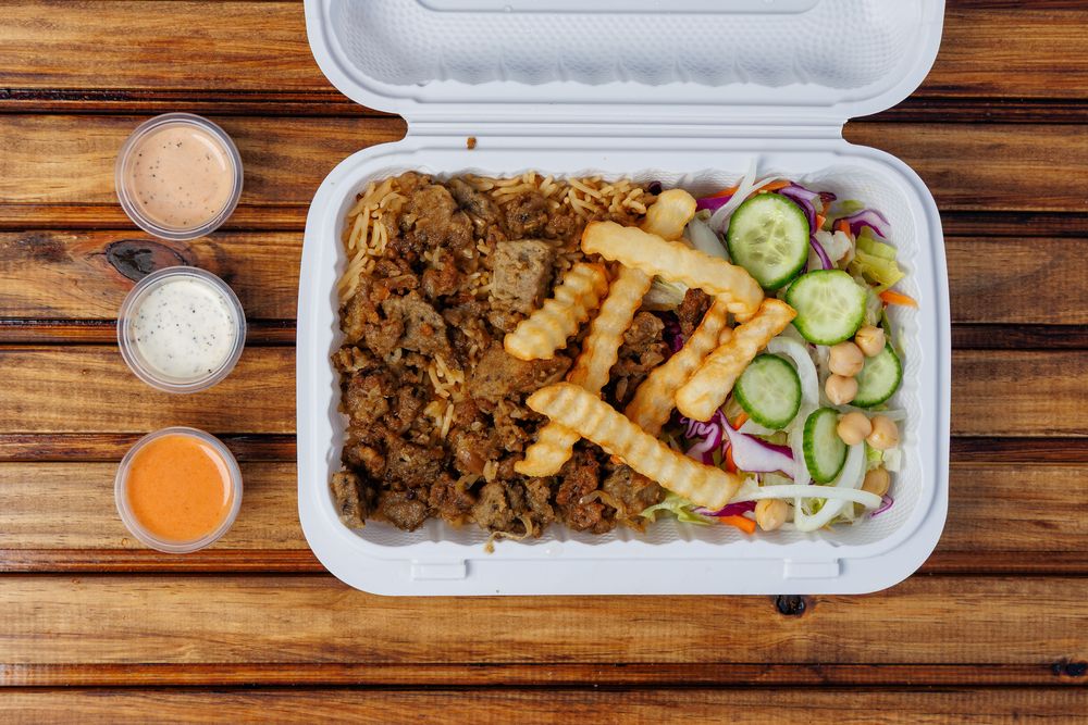 A gyro platter: meat over rice with crinkle-cut fries and a salad in a takeaway box.