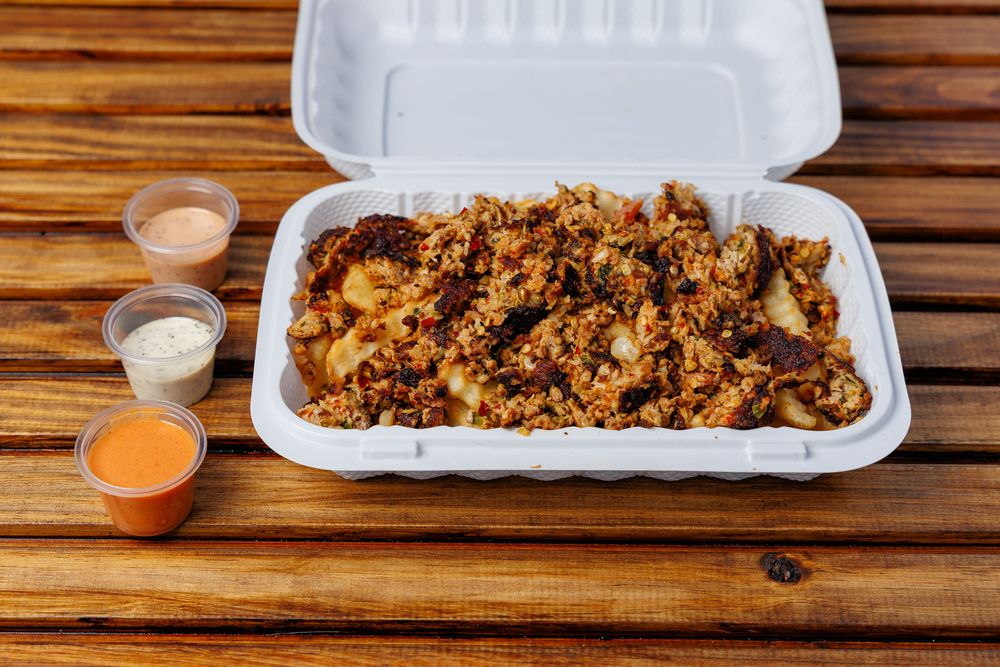 Crinkle-cut fries covered in meat in a takeaway box.