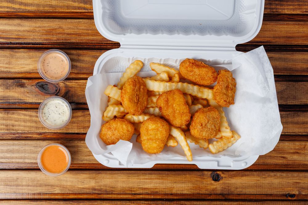 Chicken nuggets on crinkle-cut fries in a lined takeaway box with three sauce cups.