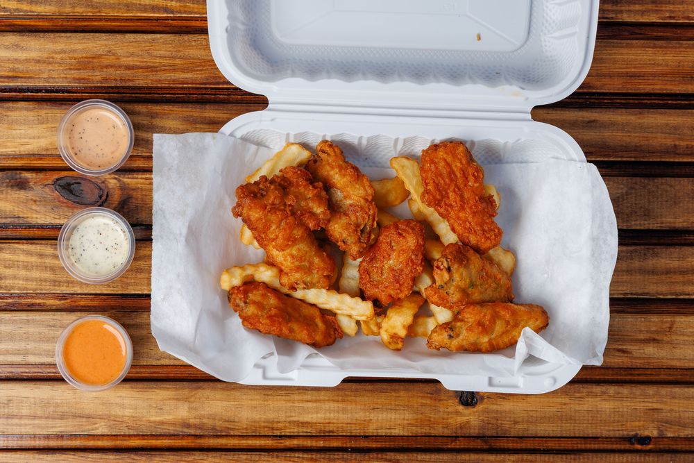 Fried chicken wings piled on crinkle-cut fries in a lined takeaway box, with three sauce cups.